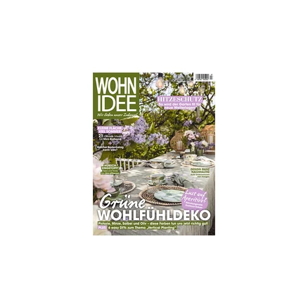 Titelseite des Magazins WOHN IDEE mit einem gedeckten Gartentisch mit grün-weißen Geschirr, geflochtenen Platzsets und Gläsern, umgeben von Fliederbüschen und Laternen. Schlagzeilen: 'HITZESCHUTZ' und 'Grüne WOHLFÜHLDEKO'.