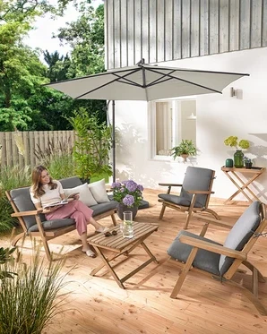 Eine Frau sitzt auf einem zusammenklappbaren Garten-Lounge-Set mit Premium-Kissen, liest und ist umgeben von einem Garten-Tabletttisch und 2 Outdoor-Kissen mit Leinen-Haptik.