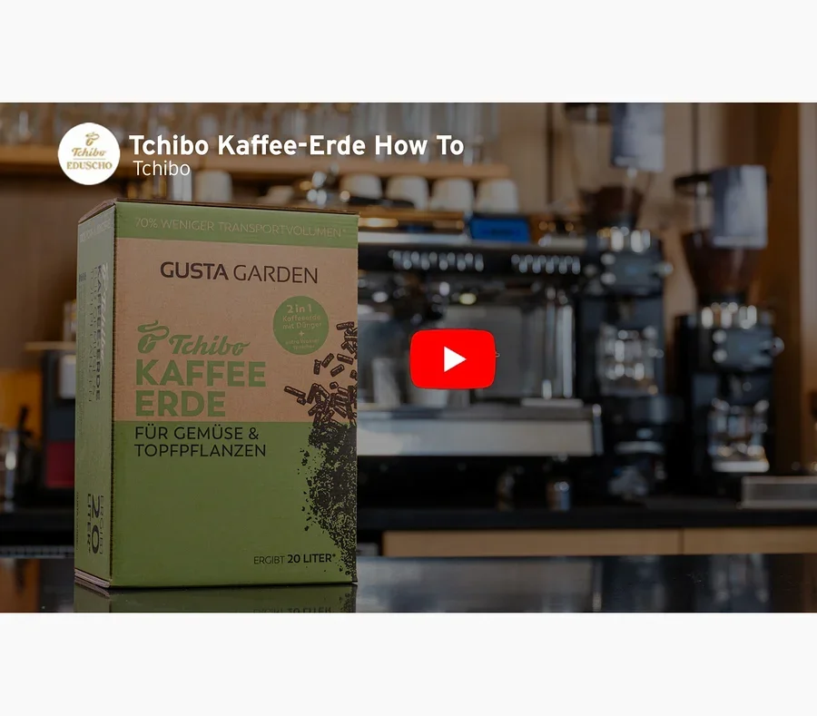 Eine Packung Tchibo Kaffee-Erde steht vor einer Kaffeemaschine. Ein roter Play-Button ist im Bild zu sehen.