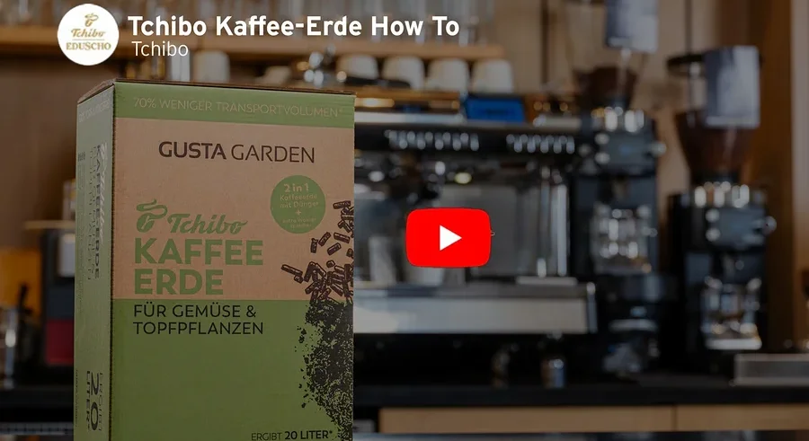 Eine Packung Tchibo Kaffee-Erde steht vor einer Kaffeemaschine. Ein roter Play-Button ist im Bild zu sehen.