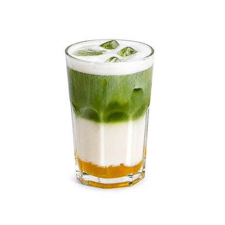 Geschichtetes Getränk in einem hohen Glas mit orangefarbener Basis, weißer Milchschicht, grüner Matcha-Schicht, weißem Schaum und grünen Eiswürfeln.