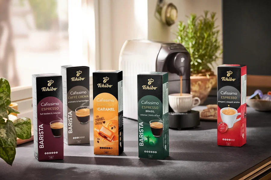 Fünf Packungen Cafissimo BARISTA Espresso Brasil Kapseln und eine Kaffeemaschine. Kaffee fließt aus der Kaffeemaschine in eine Tasse.
