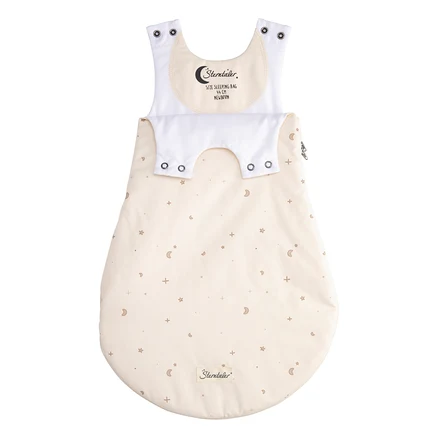 Cremefarbener Babyschlafsack mit braunen Sternen, Monden und Pluszeichen. Er hat weiße Schultergurte mit Druckknöpfen, eine weiße Druckknopfleiste und ein Etikett mit „Sterntaler, 44 cm Newborn“ auf der Brust. Ein Reißverschluss befindet sich auf der rechten Seite.