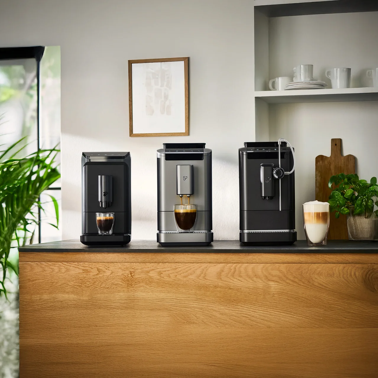 Drei Kaffeemaschinen stehen auf einer Küchentheke, wobei die mittlere Maschine Kaffee in eine Tasse ausgibt.
