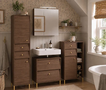Ein Badezimmer mit einem nussbaumfarbenen Hochschrank »Cottage« links, einem 60 cm breiten Waschbeckenunterschrank »Cottage« unter einem weißen Waschbecken und einem 60 cm breiten Spiegelschrank »Cottage« darüber. Rechts steht ein weiterer Hochschrank »Cottage« neben einer Badewanne.