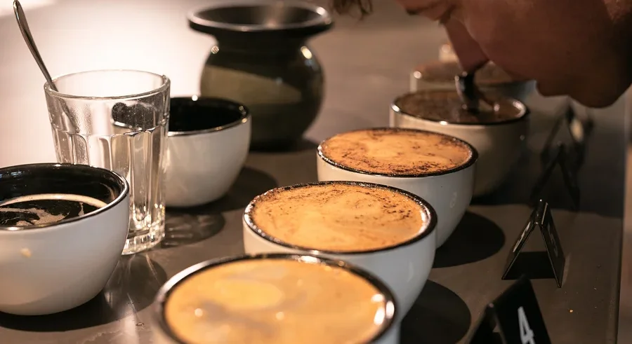 Mann riecht an einer Tasse Kaffee neben einem Glas Wasser und weiterem Kaffee.