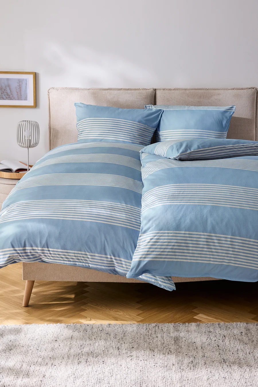 Bett mit blau-weiß gestreifter Bettwäsche und Kissen.