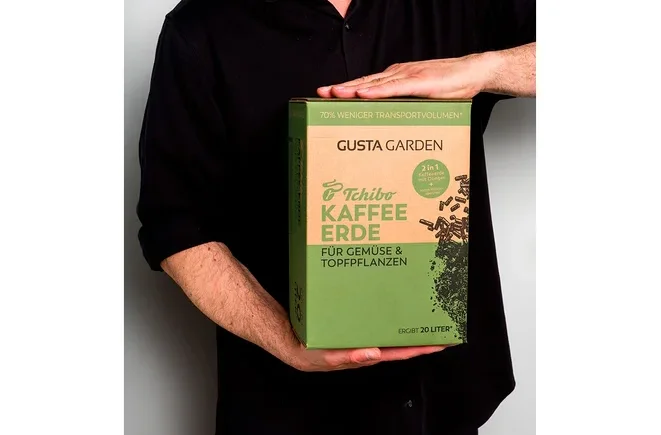 Eine Person hält eine Packung Tchibo Kaffee Erde für Gemüse und Topfpflanzen der Marke Gusta Garden.