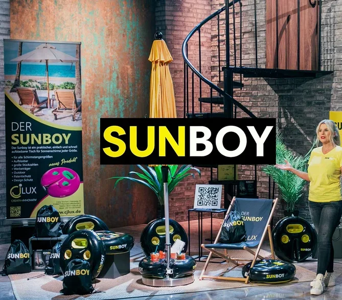 Frau präsentiert Sunboy-Produkte: aufblasbare Tische, Sonnenschirmständer, Strandstuhl und Tragetaschen vor Backsteinmauer und Wendeltreppe.
