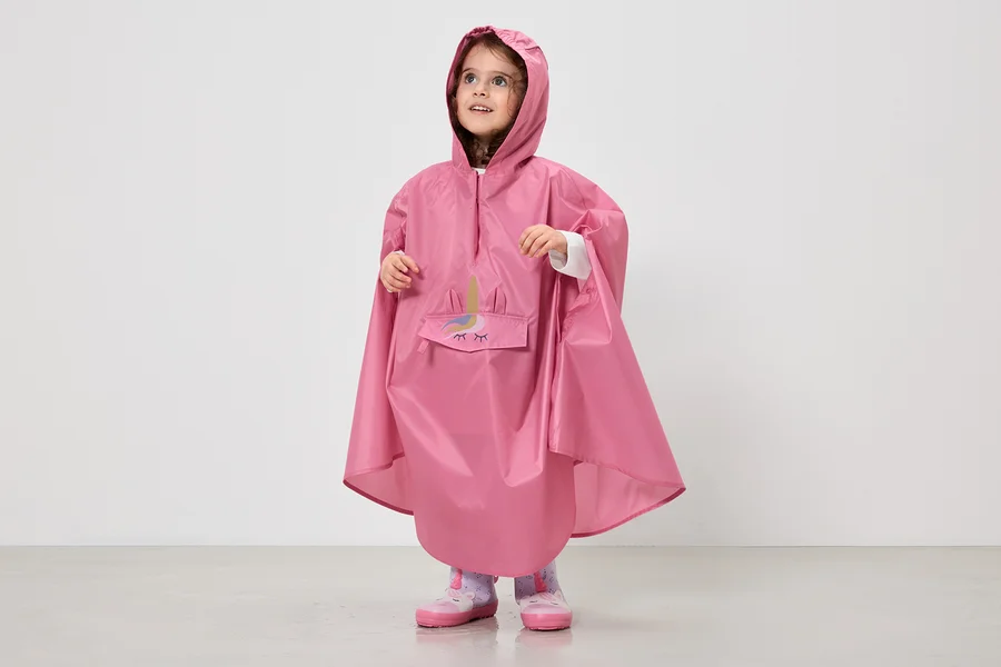 Ein kleines Mädchen trägt einen pinkfarbenen Regenponcho mit Kapuze und Einhorn-Motiv über ihrer Kleidung.