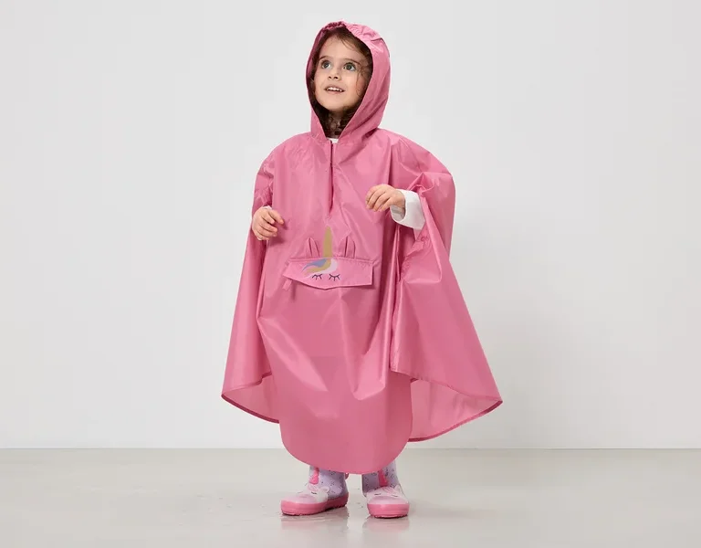 Ein kleines Mädchen trägt einen pinkfarbenen Regenponcho mit Kapuze und Einhorn-Motiv über ihrer Kleidung.