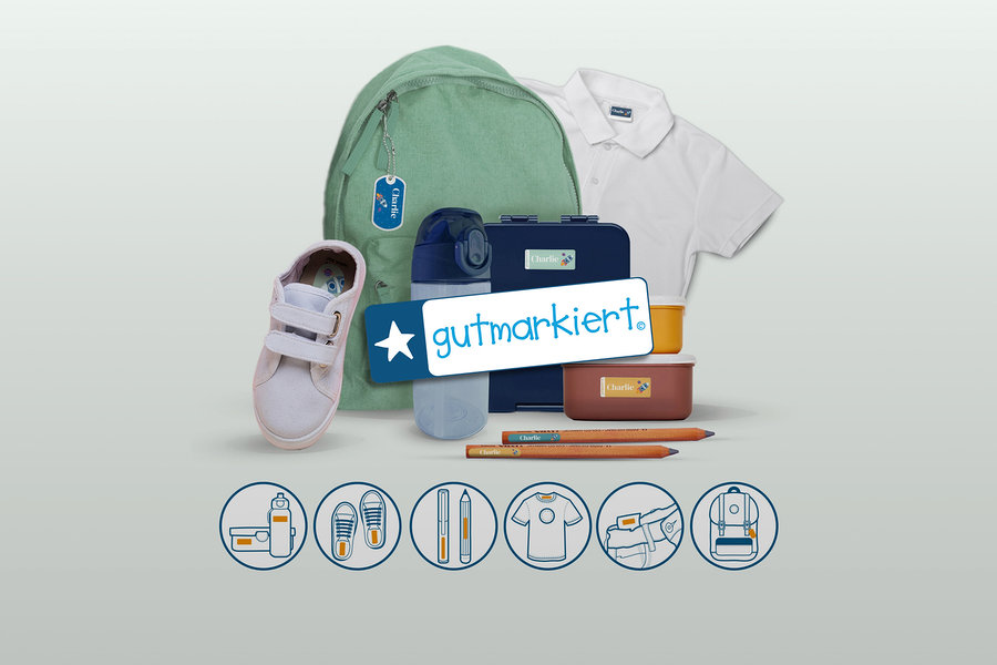 Verschiedene Schulartikel wie ein grüner Rucksack, ein weißer Schuh, eine blaue Trinkflasche, zwei Brotdosen, zwei Bleistifte und ein weißes Poloshirt sind mit personalisierten „Charlie“-Etiketten versehen. Ein „gutmarkiert.“-Logo ist mittig platziert, darunter zeigen Symbole Anwendungsbeispiele für Etiketten.