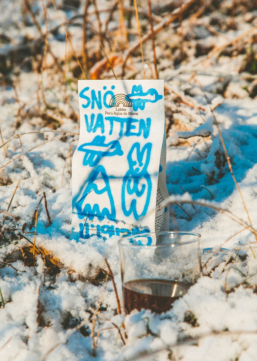 Eine Packung Lykke Peru Agua de Nieve Kaffee und ein Glas Kaffee stehen im Schnee.