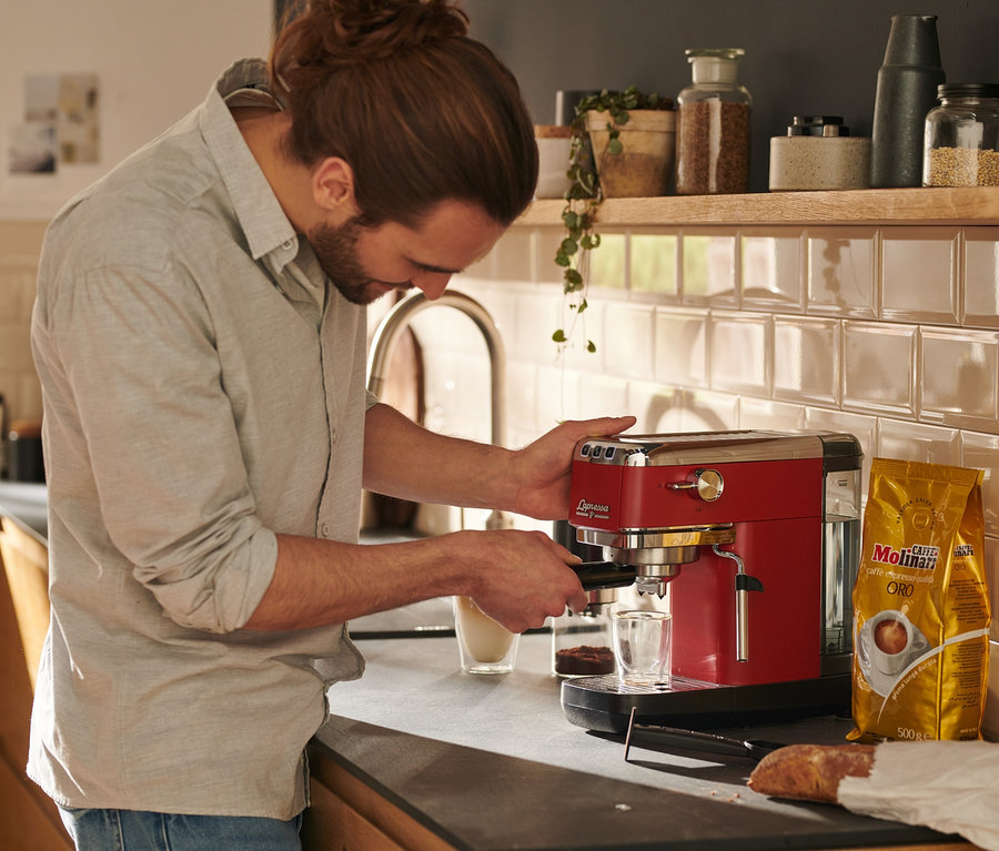 Mann bereitet mit einer roten »Lapressa« Siebträgermaschine Kaffee zu.
