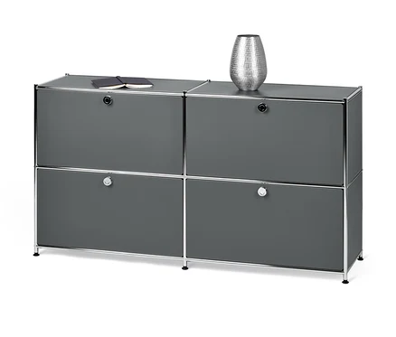 Ein graues Sideboard Metall »CN3« mit 4 Klappfächern. Oben liegen ein Notizbuch und eine silberne Vase.