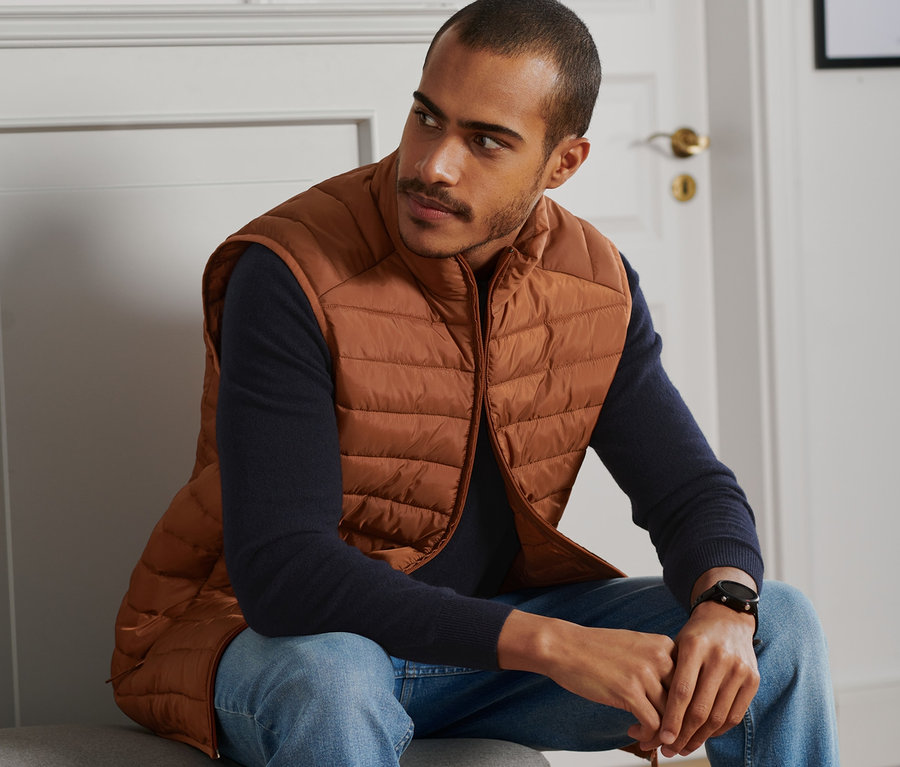 Mann sitzt und trägt eine cognacfarbene Steppweste.