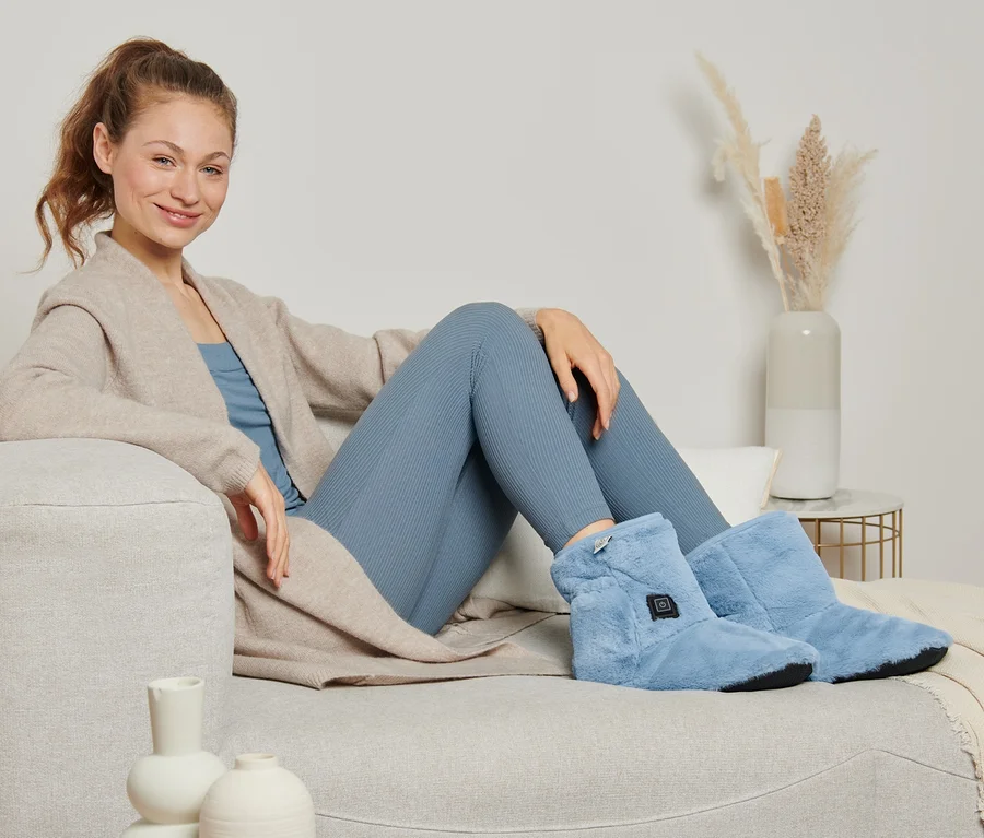 Eine Frau sitzt auf einem Sofa und trägt beheizbare Schuhe.