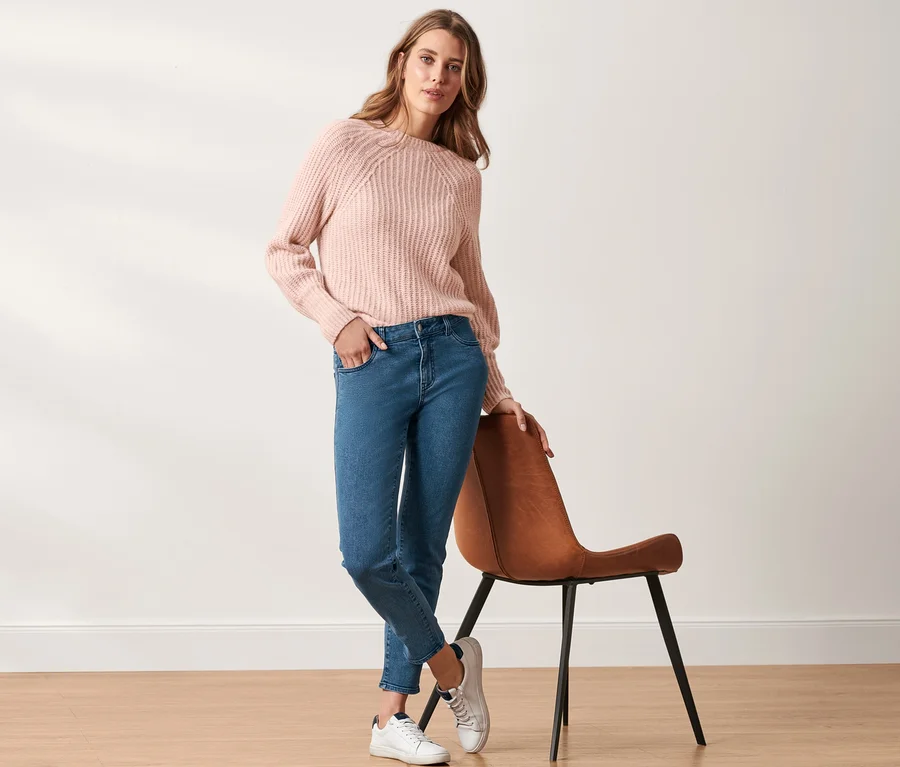 Frau posiert in einem rosa Pullover und Slimfit-Jeans.