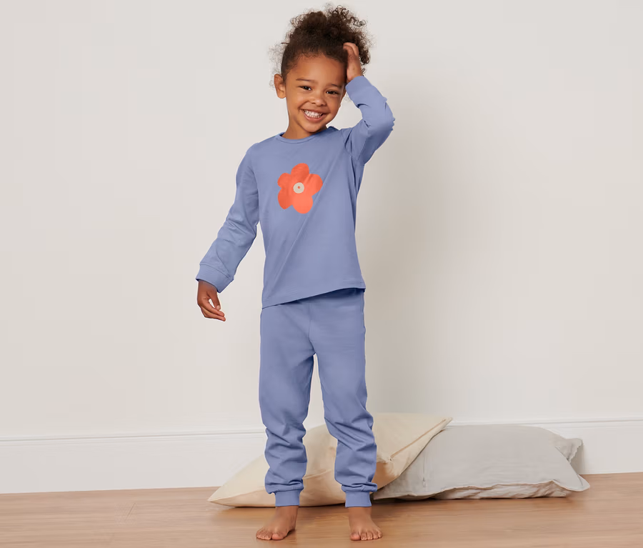 Lächelndes kleines Mädchen im Kleinkind-Pyjama posiert auf dem Boden mit Kissen.