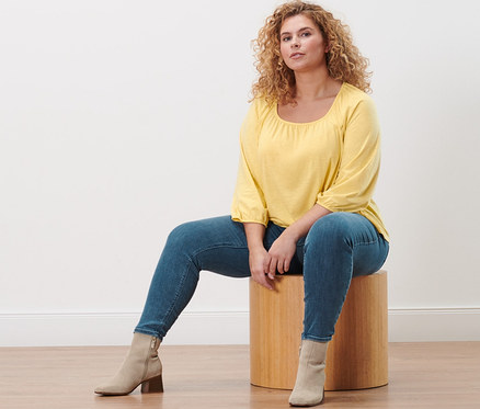 Eine Frau sitzt auf einem Hocker und trägt ein gelbes Blusenshirt mit 3/4-Arm und Treggings »Fit Nelly«.
