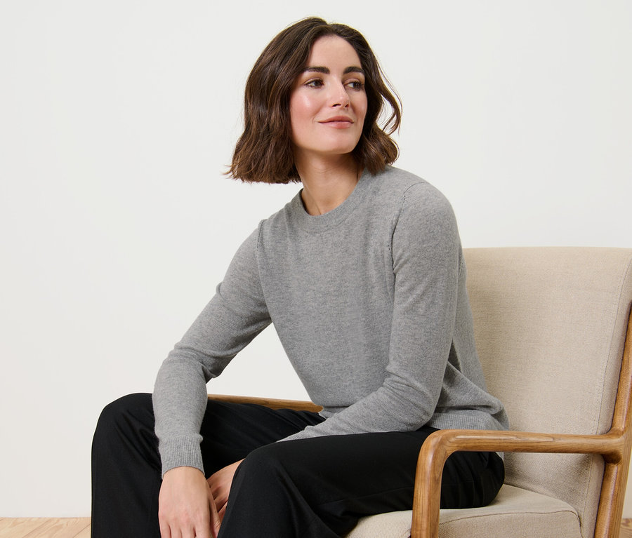 Frau sitzt im Sessel und trägt einen grau melierten Feinstrickpullover mit Cashmere.