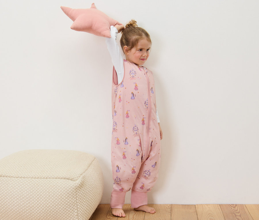 Mädchen hält ein rosa sternförmiges Kissen und trägt einen rosa Schlafsack mit Beinen, 2,5 TOG, ca. 110 cm.