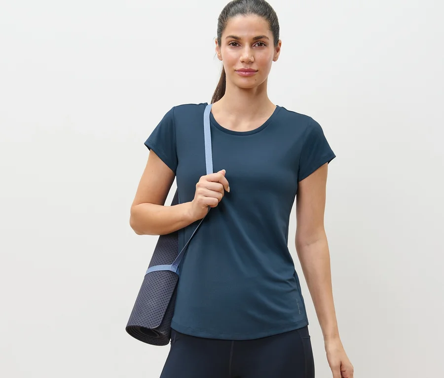 Frau trägt blaues Funktionsshirt und trägt eine Yogamatte.