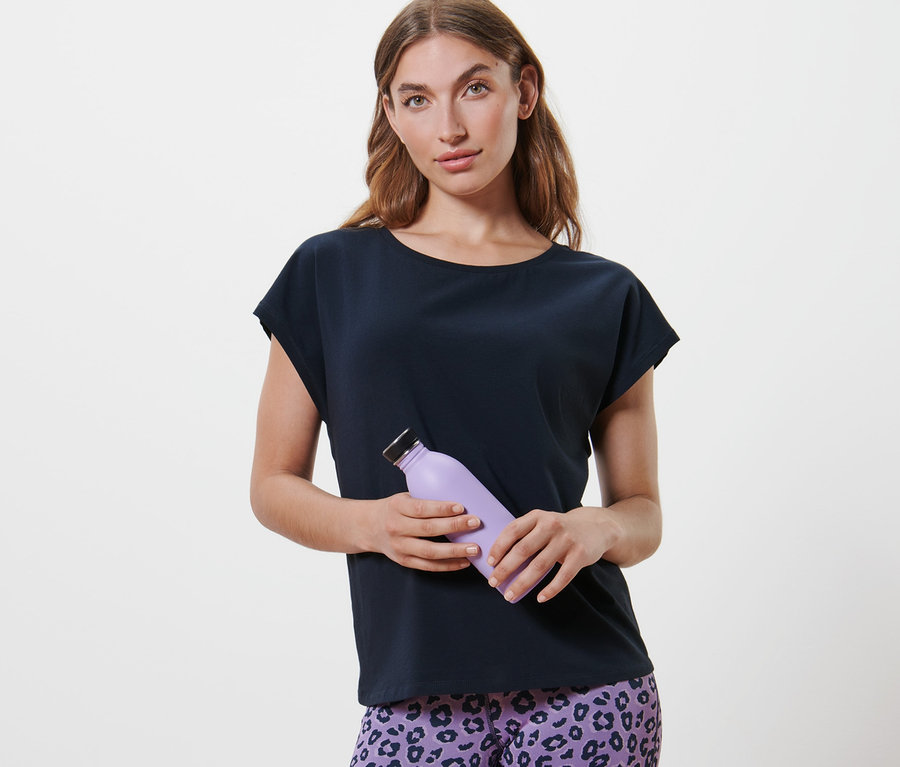 Frau hält eine lila Wasserflasche und trägt ein dunkelblaues Sportshirt.