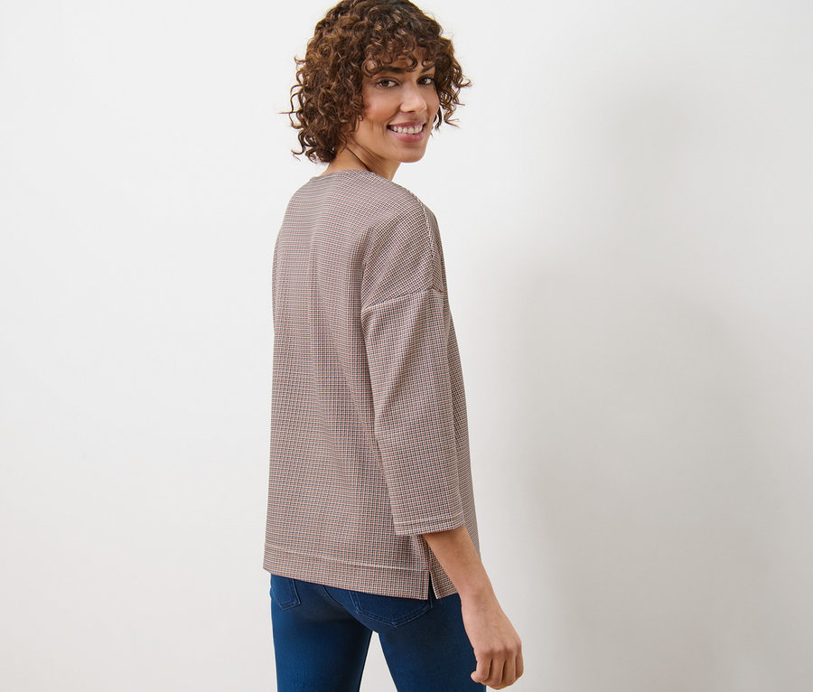 Frau blickt über die Schulter und trägt ein kariertes Sweatshirt und Jeans.