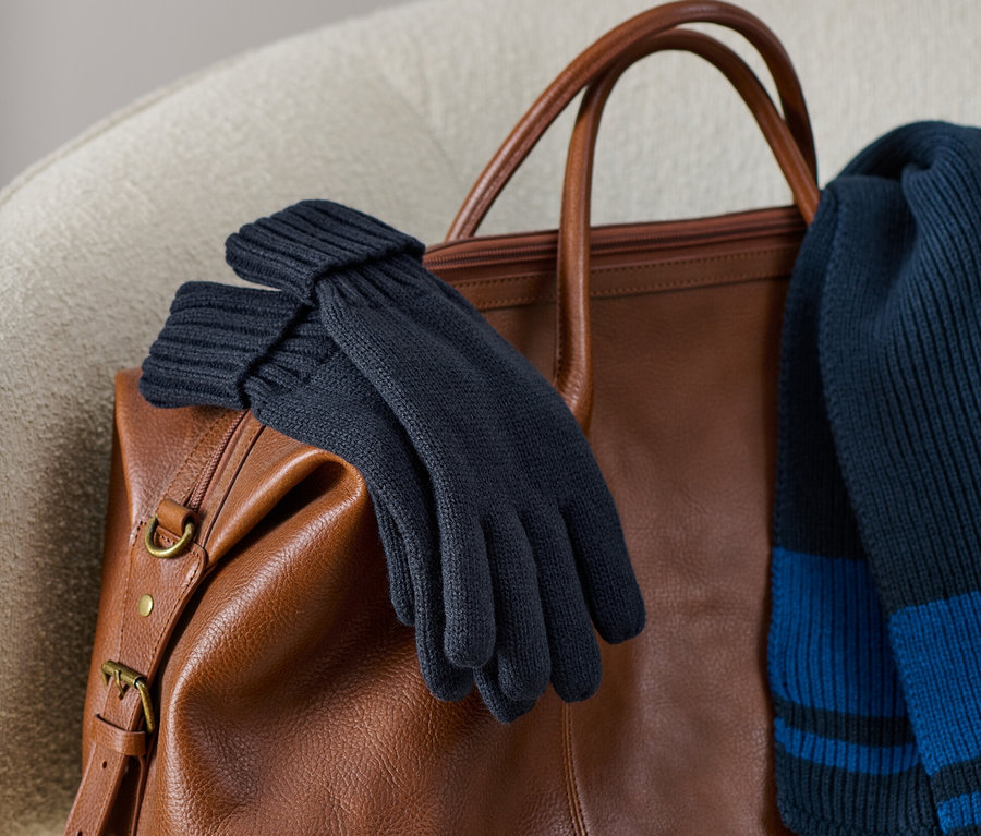 Strickhandschuhe liegen auf einer braunen Ledertasche zusammen mit einem Strickschal.