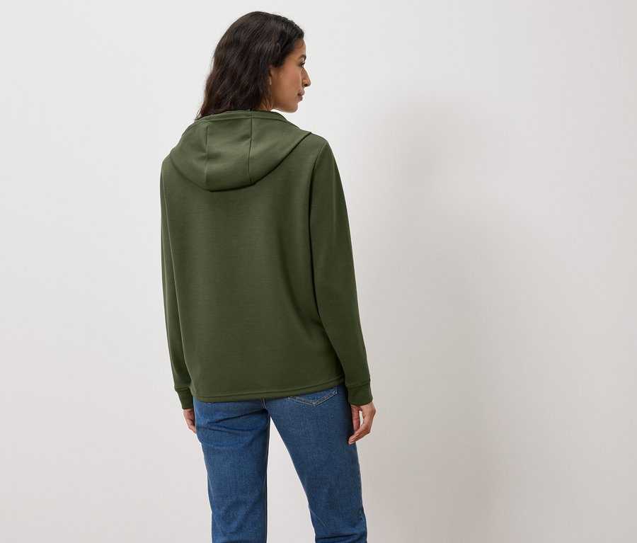 Frau mit dem Rücken zur Kamera trägt einen grünen Hoodie und Jeans.