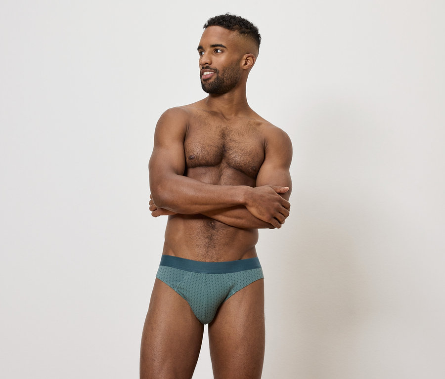 Mann mit verschränkten Armen vor der Brust, der eine grüne Herrenunterhose trägt.