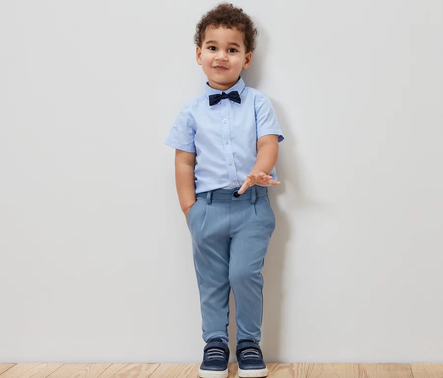 Junge mit blauem Hemd, Fliege und Kinder-Chinohose.