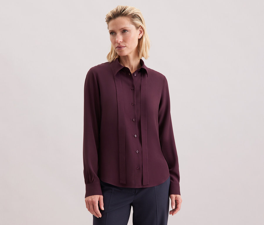 Frau trägt eine Seidensticker Schluppenbluse aus Viskose, bordeauxrot, mit Knöpfen.