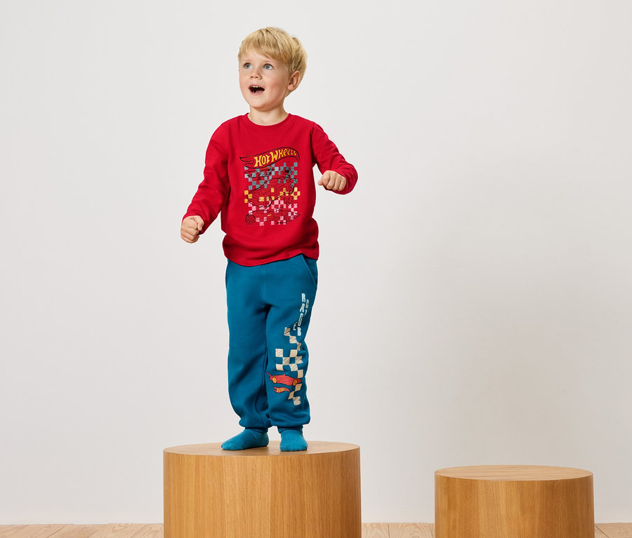Junge steht auf einem Holzsockel in rotem T-Shirt und blauen Hosen.