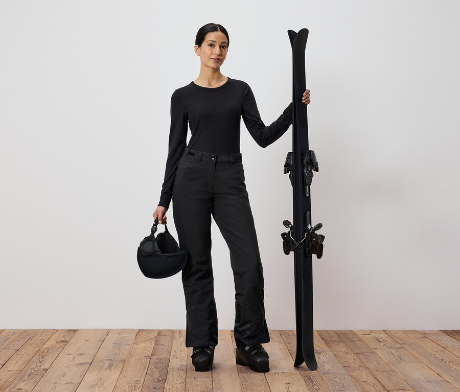 Frau in schwarzer Skibekleidung hält Ski und Helm.