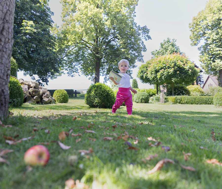 Ein Kind in pinkfarbener Hose geht auf einer Wiese im Garten.
