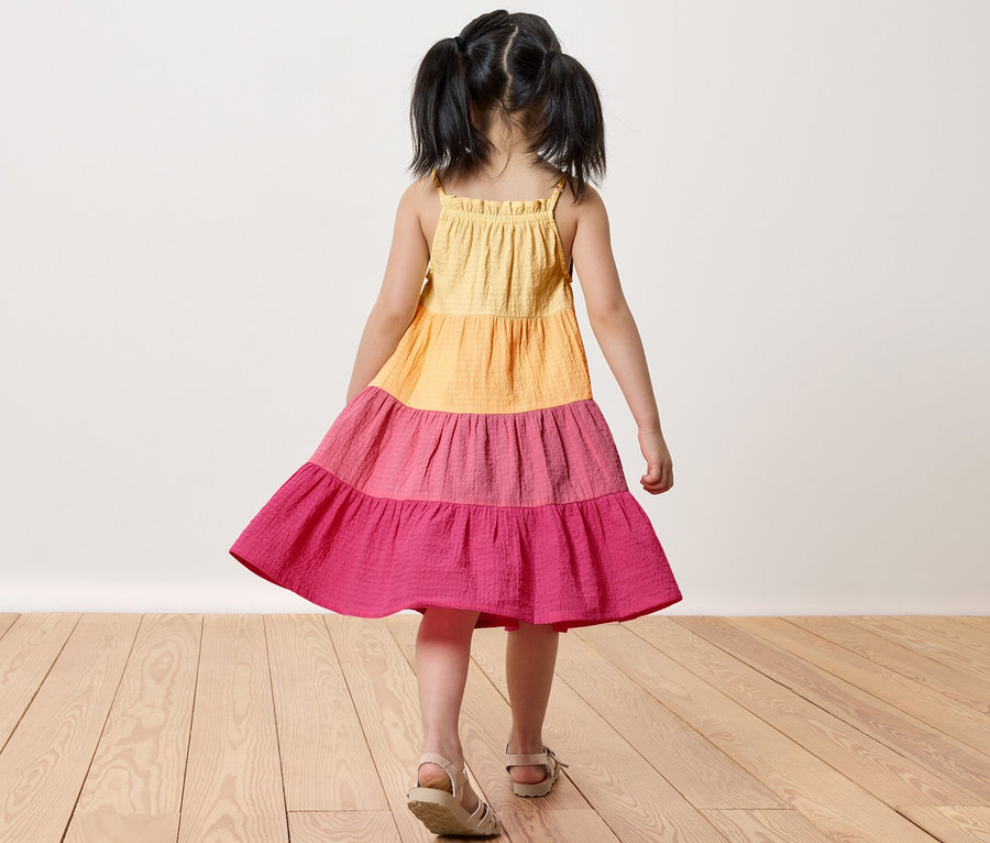 Mädchen im Kinder-Webkleid steht auf Holzboden.