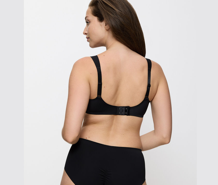 Rückansicht einer Frau mit braunen Haaren, die einen schwarzen Triumph Essential »Minimizer W X« BH und schwarze Unterwäsche trägt.