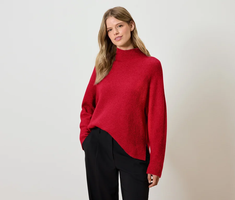 Frau posiert in rotem Pullover und schwarzer Hose.