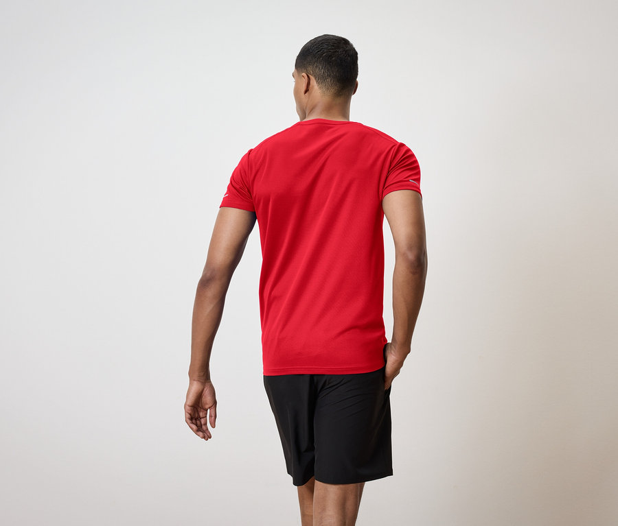 Ein Mann mit dem Rücken zur Kamera trägt ein rotes T-Shirt und schwarze Shorts.