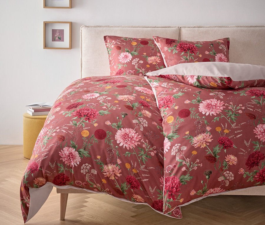 Blumenbettwäsche auf einem Bett mit Kissen und Nachttisch.