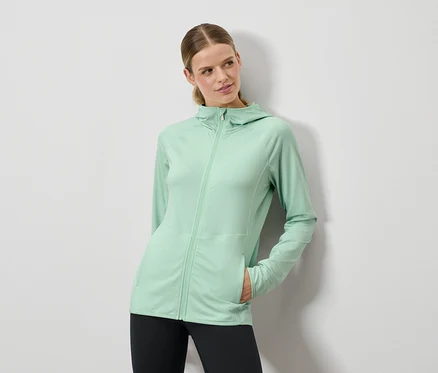 Frau posiert in mintgrüner Kapuzenjacke und schwarzen Leggings.