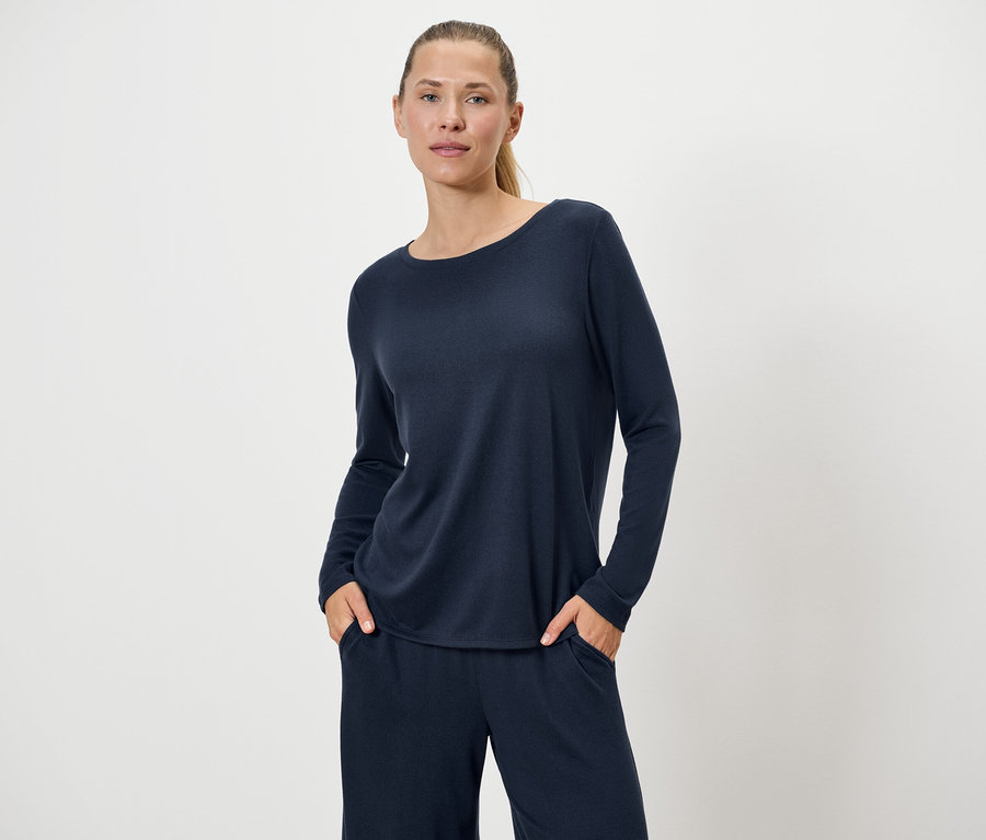 Frau in marineblauem Pullover und Hose posiert vor einem weißen Hintergrund.