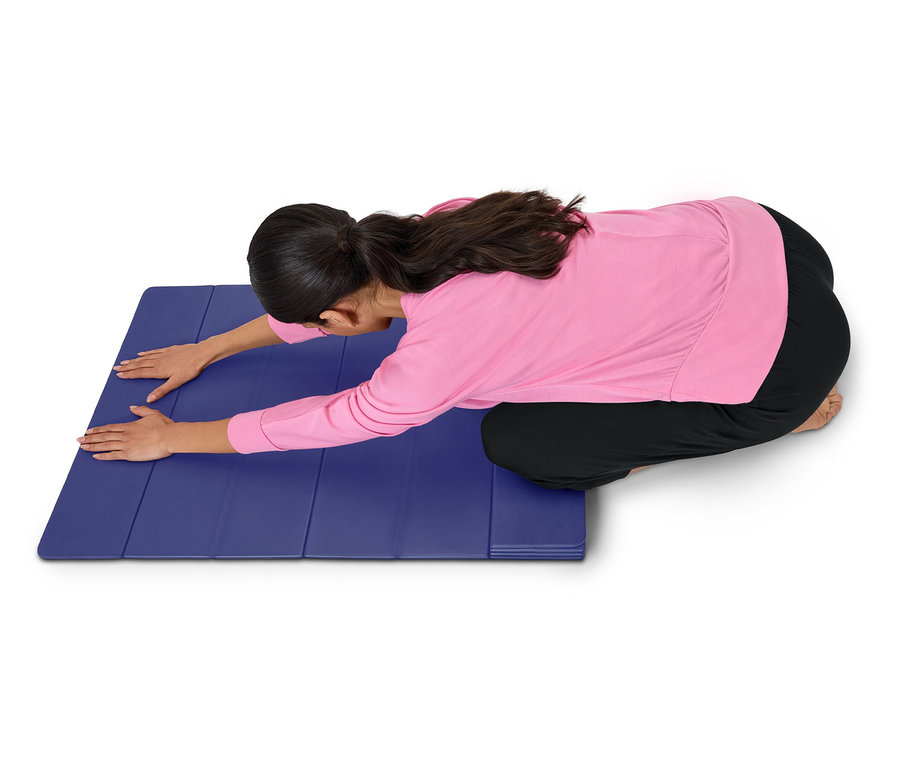 Frau in rosa Oberteil und schwarzen Hosen dehnt sich auf einer blauen Matte.