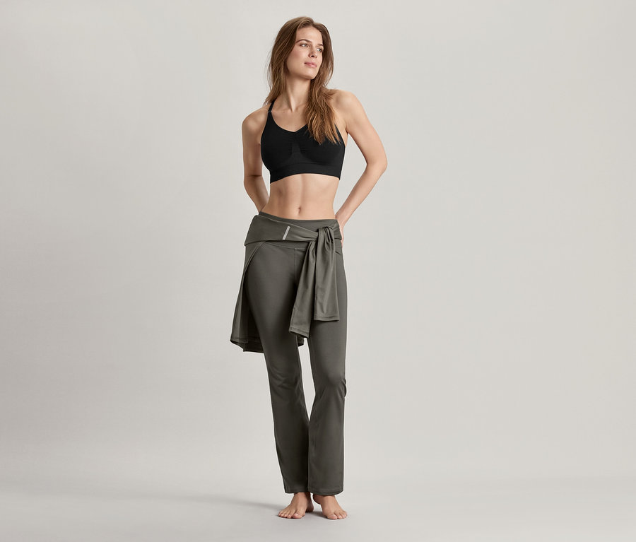 Frau trägt Seamless-Sport-Bustier, schwarz und Bodyforming-Sporthose, olivgrün.