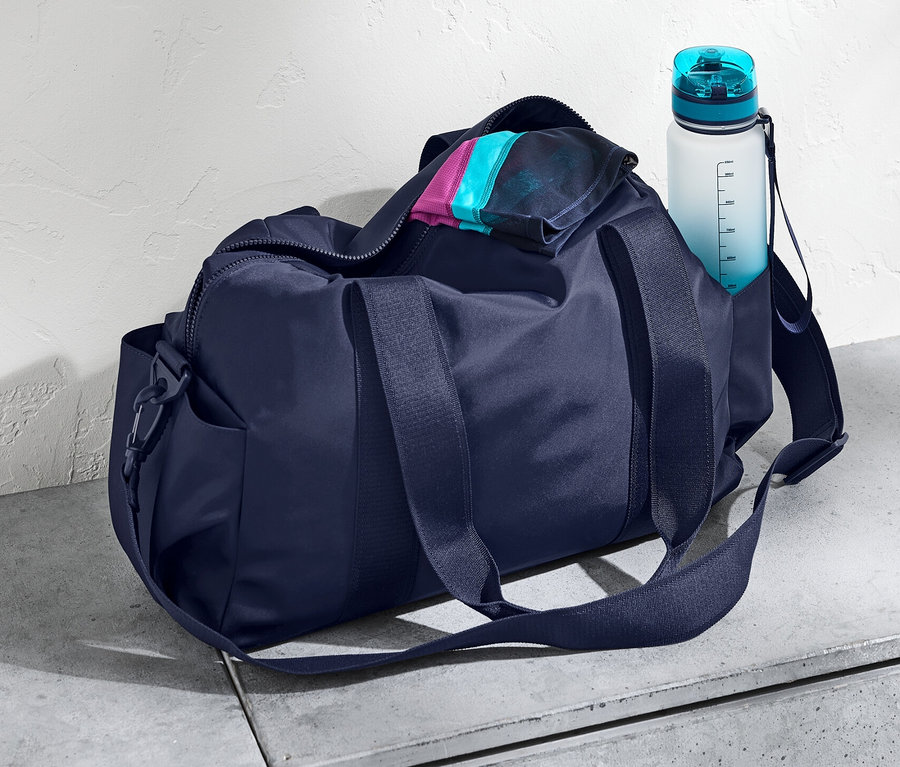 Eine dunkelblaue Sporttasche und eine Wasserflasche auf einer Betonoberfläche.