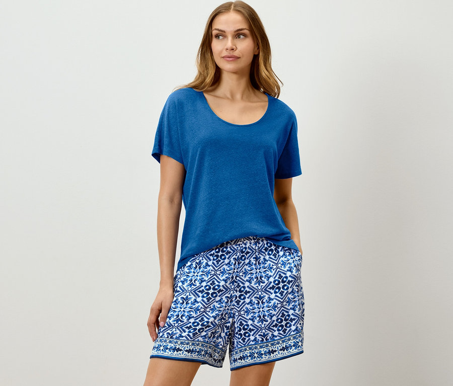 Frau trägt kobaltblaues Leinenmisch-Shirt und blaue gemusterte Shorts.