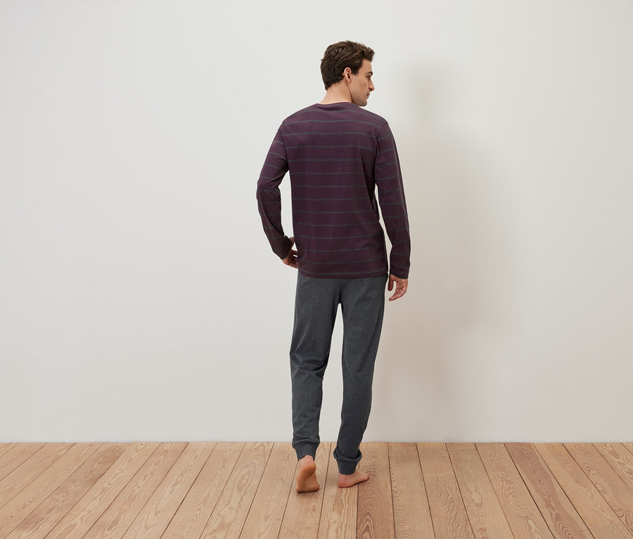 Mann von hinten, bekleidet mit einem gestreiften Langarmshirt und grauer Jogginghose, steht auf einem Holzboden.