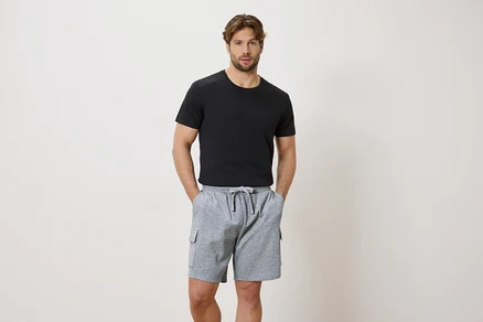 Mann mit Händen in den Taschen einer grauen Kordelzugshorts und einem schwarzen Kurzarm-T-Shirt.